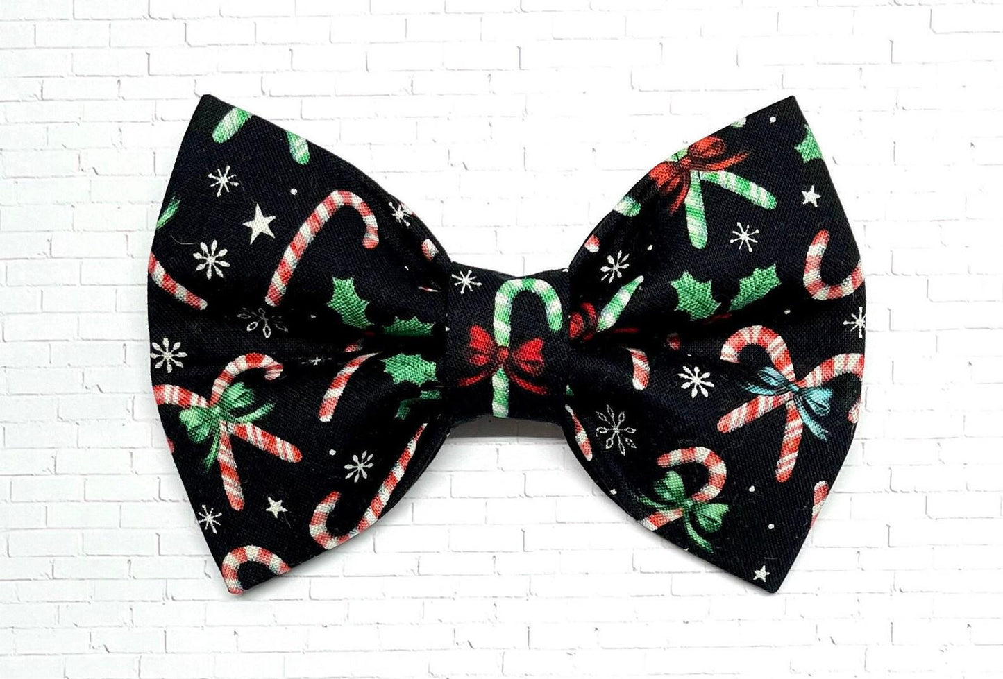 Black Christmas dog bow tie decorated with red, green, and white candy cane designs, displayed on a white background. The handmade bow tie features a festive holiday pattern.