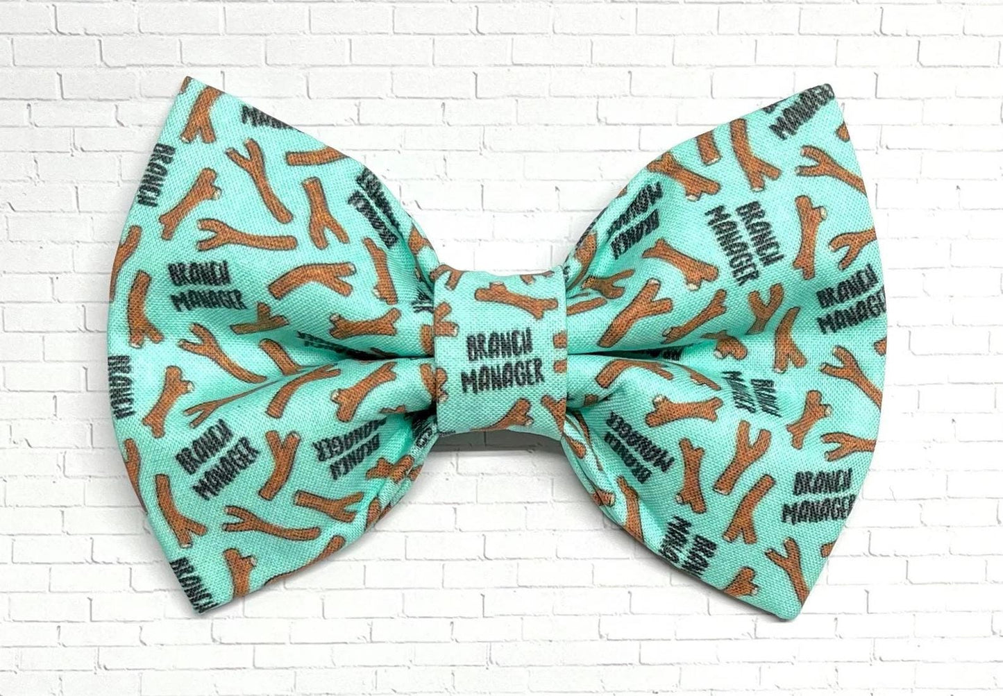Mint green dog bow tie featuring a repeating pattern of brown sticks and the phrase “Branch Manager,” perfect for playful pups who love fetch.