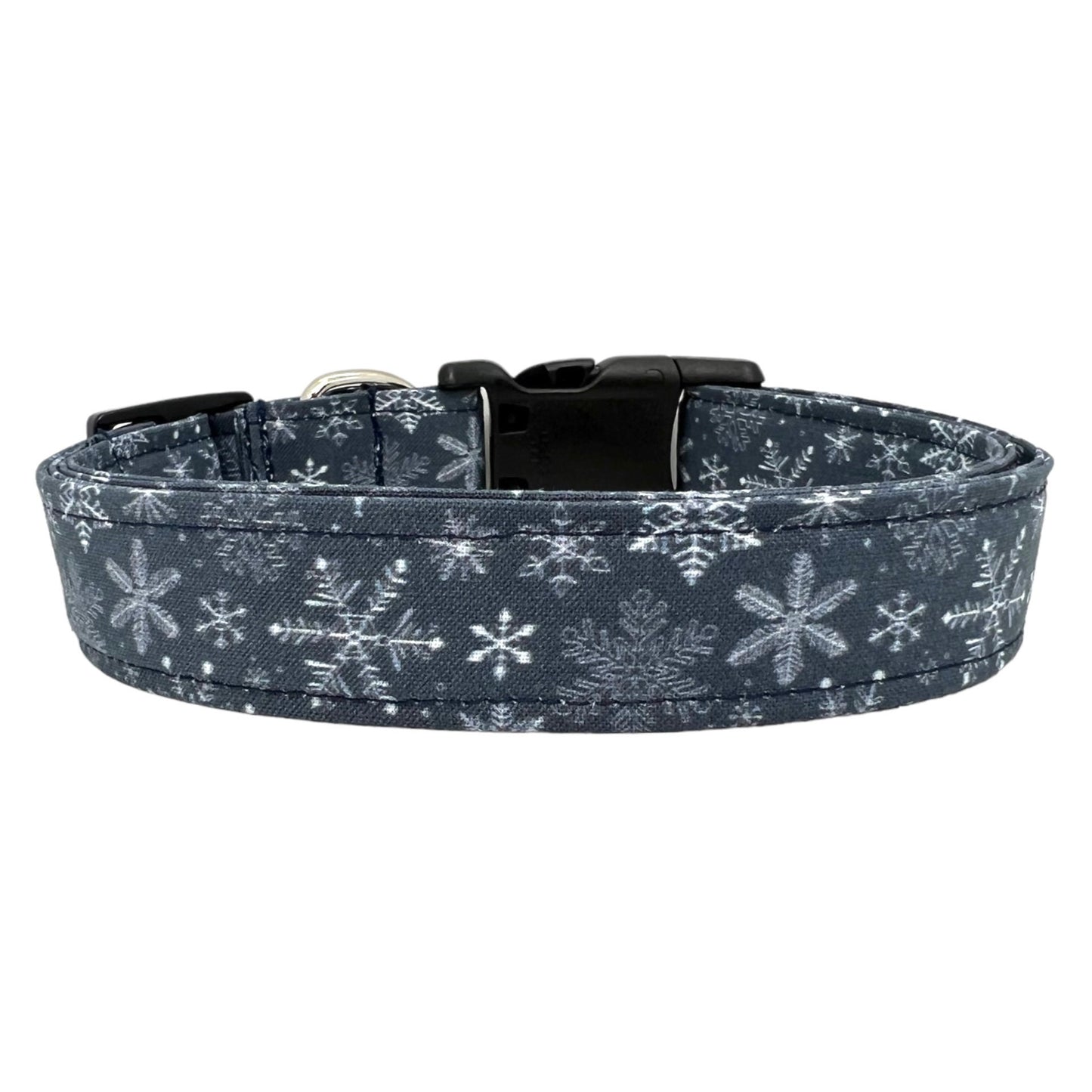 Navy blue dog collar decorated with white snowflakes scattered across the fabric, shown flat to highlight the crisp winter pattern.