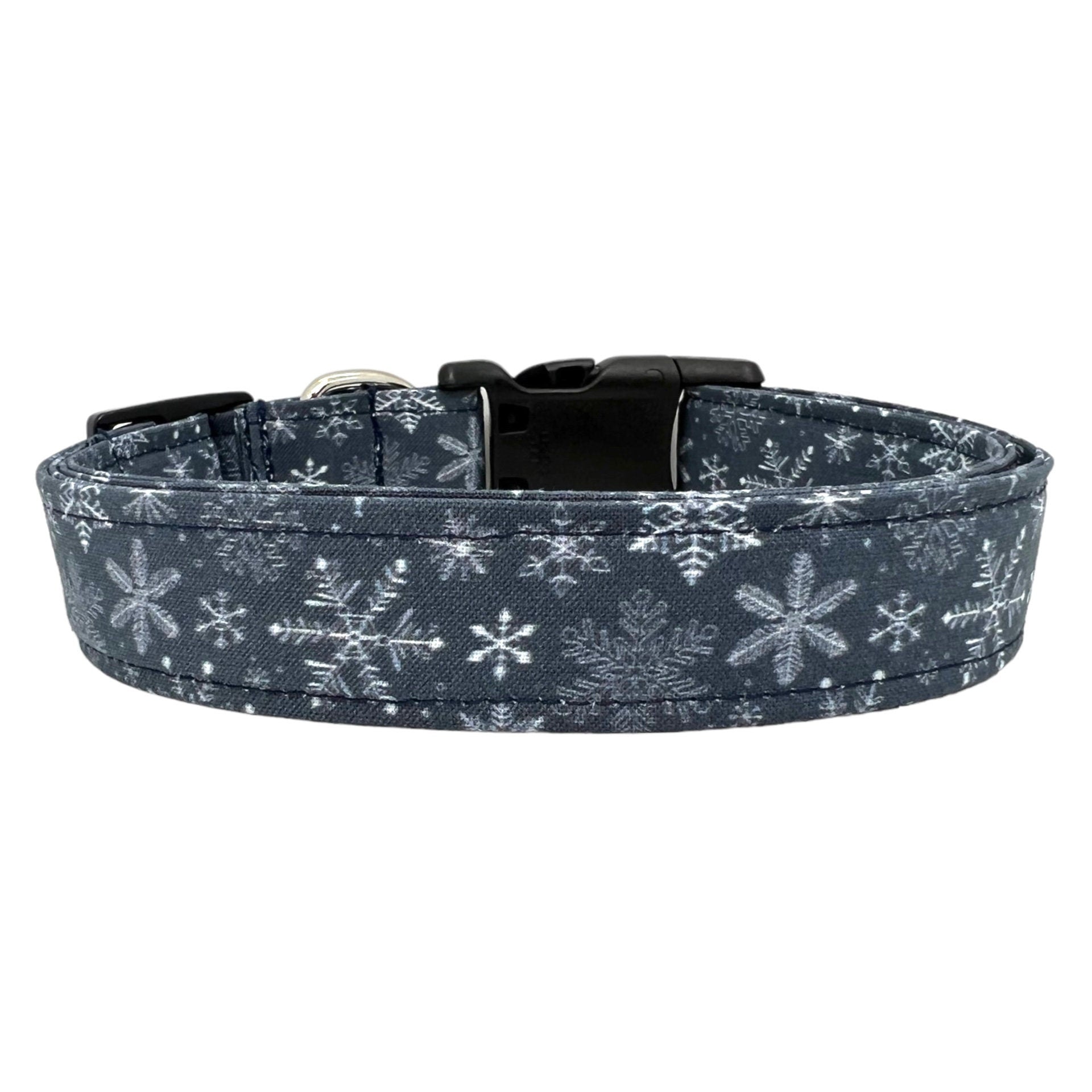 Navy blue dog collar decorated with white snowflakes scattered across the fabric, shown flat to highlight the crisp winter pattern.