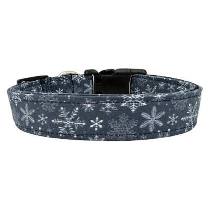 Navy blue dog collar decorated with white snowflakes scattered across the fabric, shown flat to highlight the crisp winter pattern.