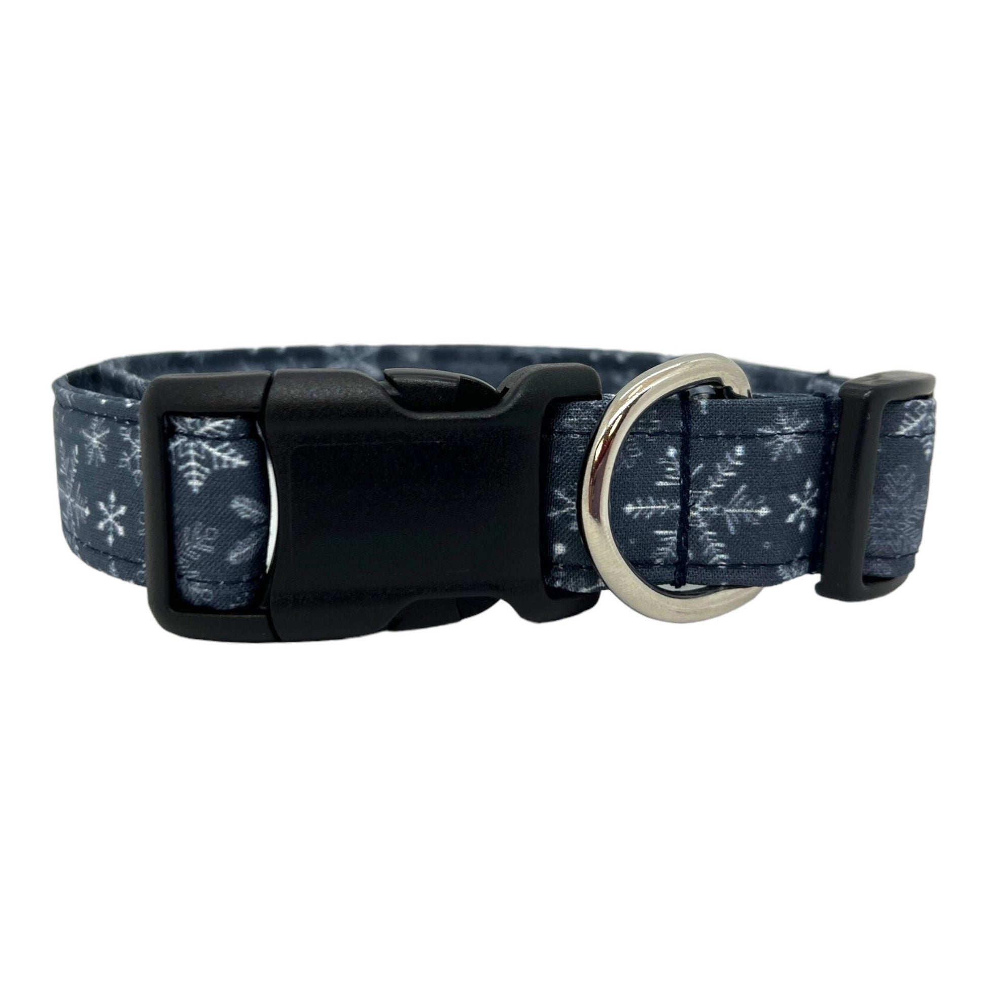 Navy blue dog collar decorated with white snowflakes scattered across the fabric, shown flat to highlight the crisp winter pattern.