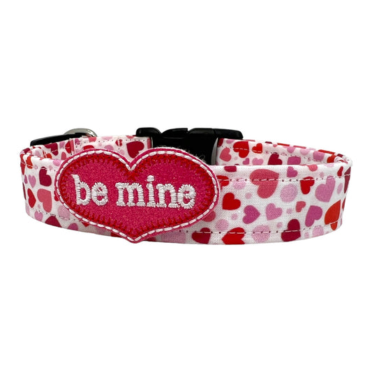 Valentine’s Day dog collar featuring red and pink hearts in various sizes, with be mine heart shaped dog collar embellishment. Heart-themed dog collar shown flat.