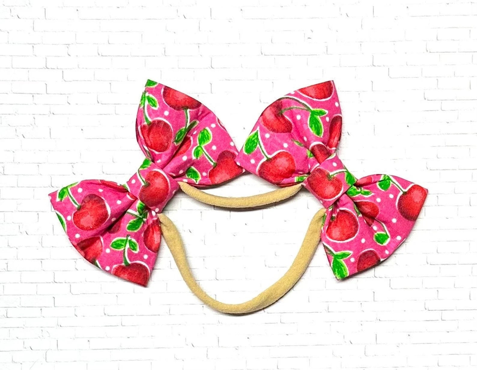 Pink cherry dog bow headband featuring two handmade bows on a soft, stretchy nylon band, designed for a comfortable and secure fit on dogs of all sizes.
