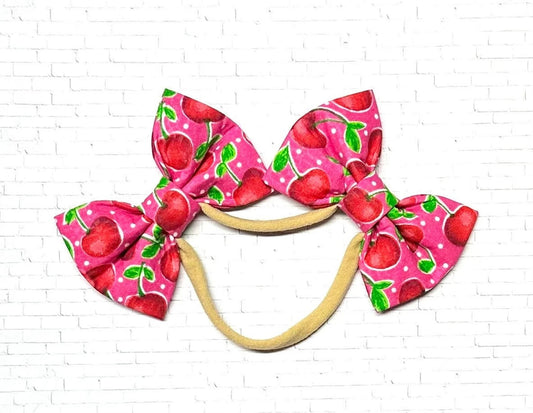 Pink cherry dog bow headband featuring two handmade bows on a soft, stretchy nylon band, designed for a comfortable and secure fit on dogs of all sizes.