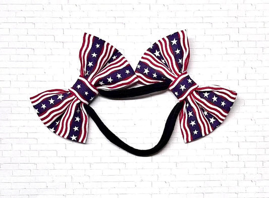 Patriotic dog headband with two red, white, and blue bows in a stars and stripes pattern on a soft nylon band, perfect for a dog for a festive Fourth of July look.