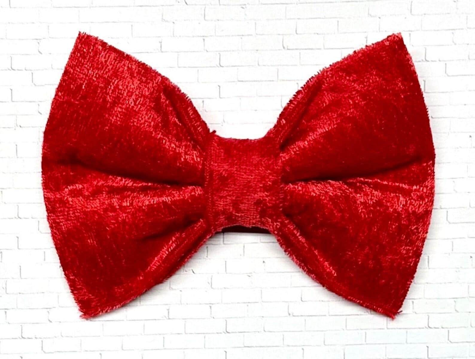Red velvet dog bow tie with a soft, plush texture, displayed on a white background. The elegant accessory features a deep red hue and  elastic loops on the back for easy attachment.