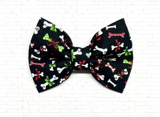 Black Christmas dog bow tie with colorful holiday dog bone pattern, displayed on a white background. The festive bow tie features red, green, and white bones wrapped as Christmas presents.
