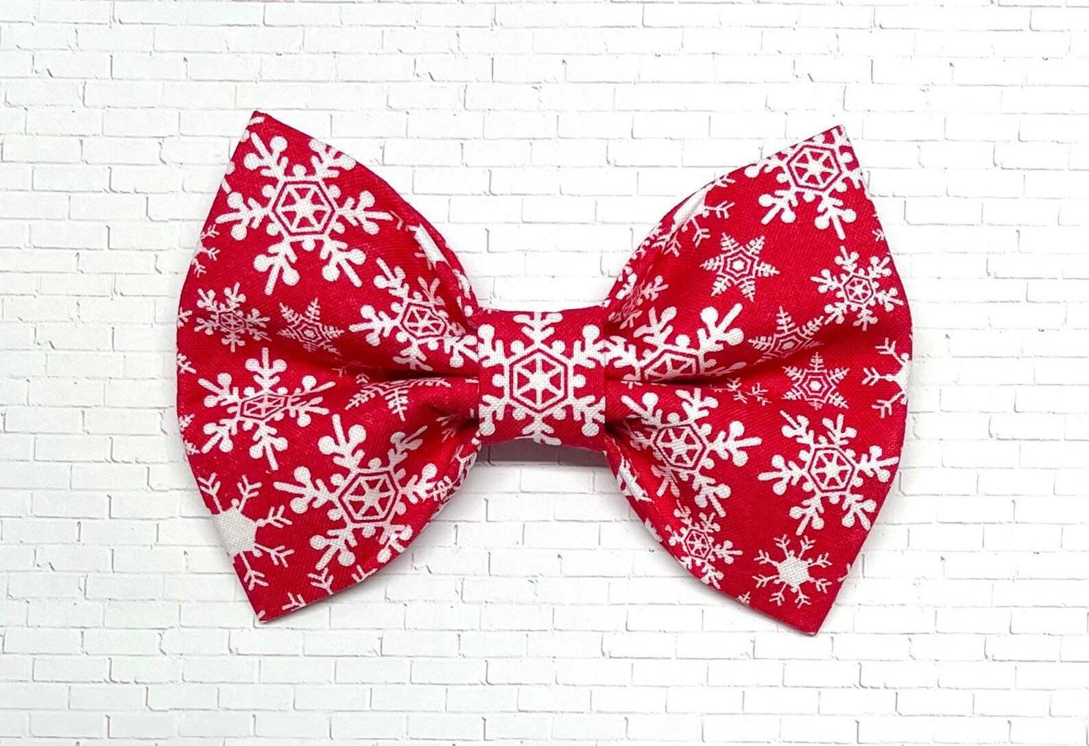 Red dog bow tie with a white snowflake pattern, displayed on a white background. The festive bow tie features elastic loops on the back for easy attachment to a dog collar.