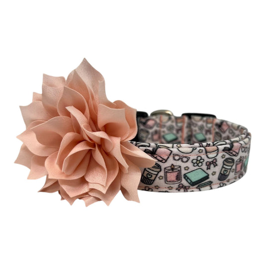 Pale pink dog collar with whimsical illustrations of books, coffee cups, candles, daisies, bows, and glasses, paired with a removable flower attached by an elastic loop.