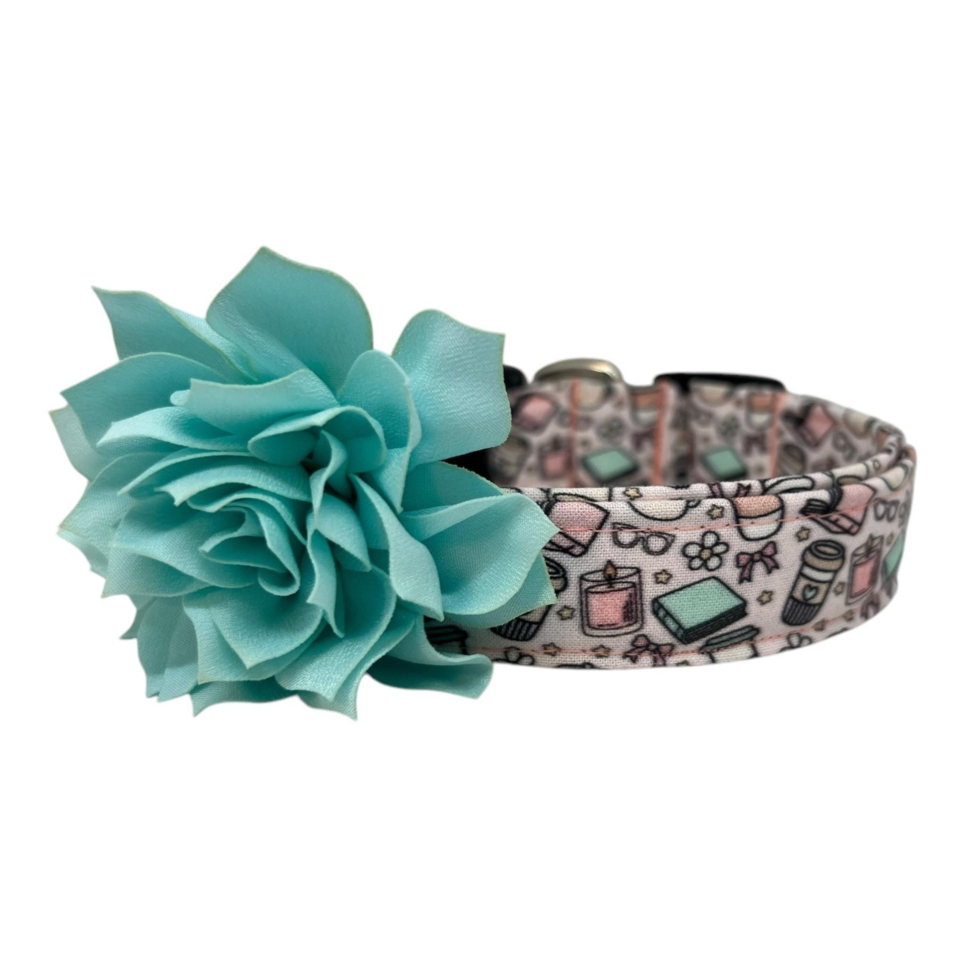 Pale pink dog collar with whimsical illustrations of books, coffee cups, candles, daisies, bows, and glasses, paired with a removable flower attached by an elastic loop.