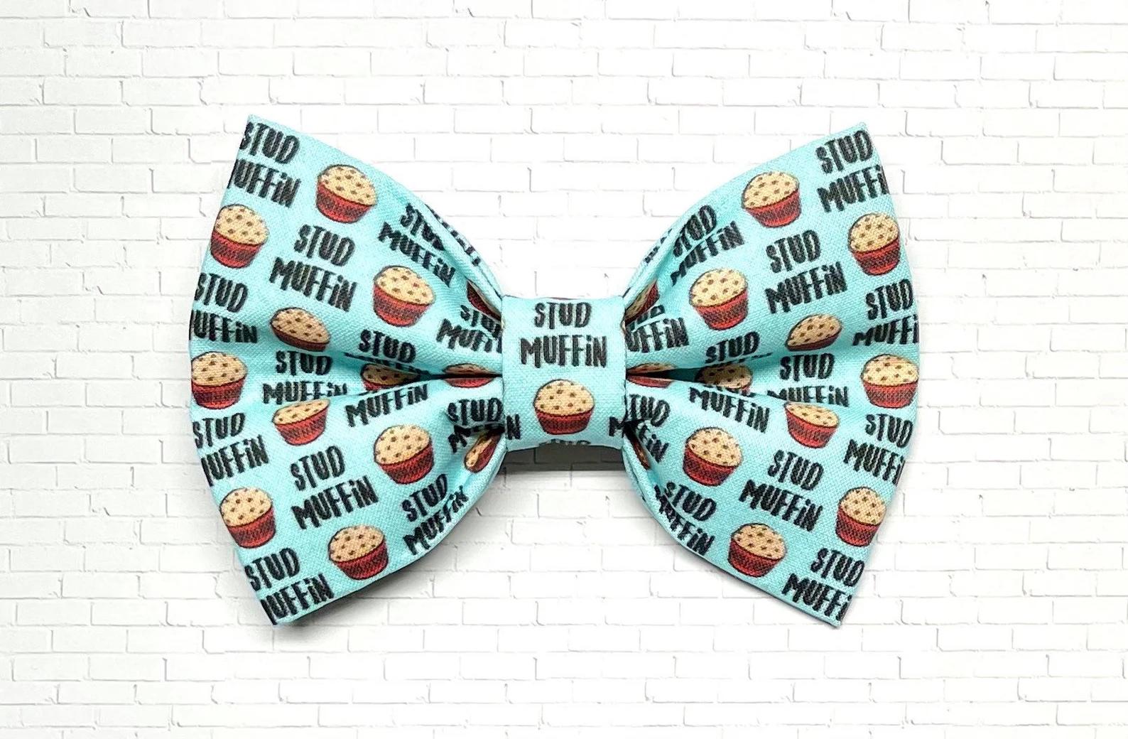 Light blue dog bow tie with a playful “Stud Muffin” pattern featuring cartoon muffins, perfect for charming pups with big confidence.