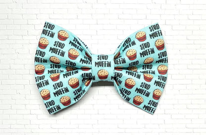 Light blue dog bow tie with a playful “Stud Muffin” pattern featuring cartoon muffins, perfect for charming pups with big confidence.