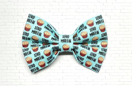 Light blue dog bow tie with a playful “Stud Muffin” pattern featuring cartoon muffins, perfect for charming pups with big confidence.