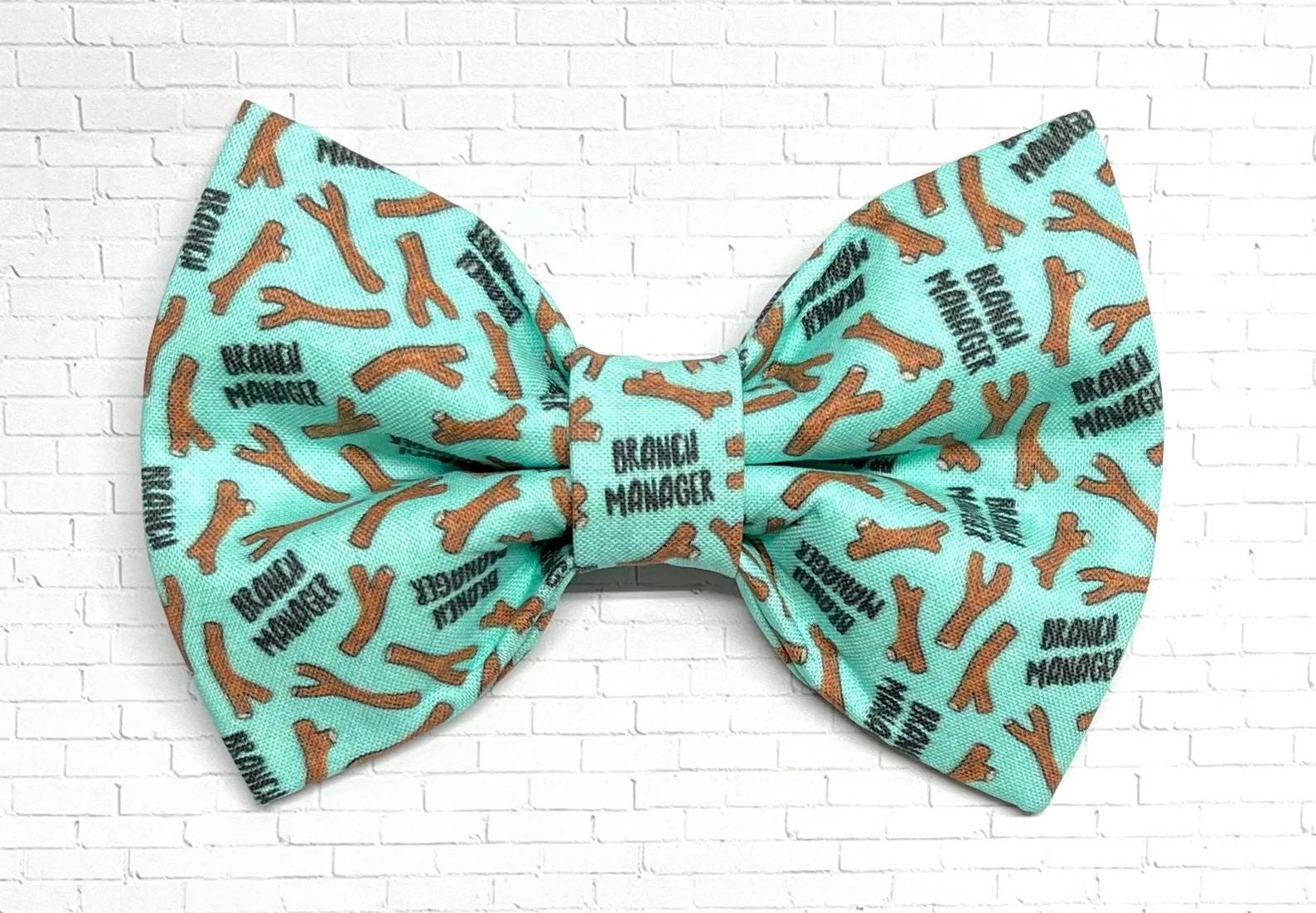 Mint green dog bow tie featuring a repeating pattern of brown sticks and the phrase “Branch Manager,” perfect for playful pups who love fetch.