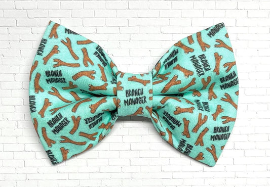 Mint green dog bow tie featuring a repeating pattern of brown sticks and the phrase “Branch Manager,” perfect for playful pups who love fetch.