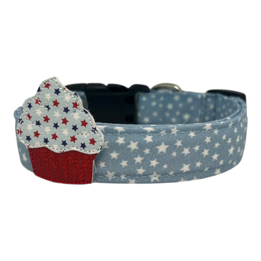Light blue chambray dog collar with scattered white stars, paired with a removable patriotic cupcake embellishment in red, white, and blue.