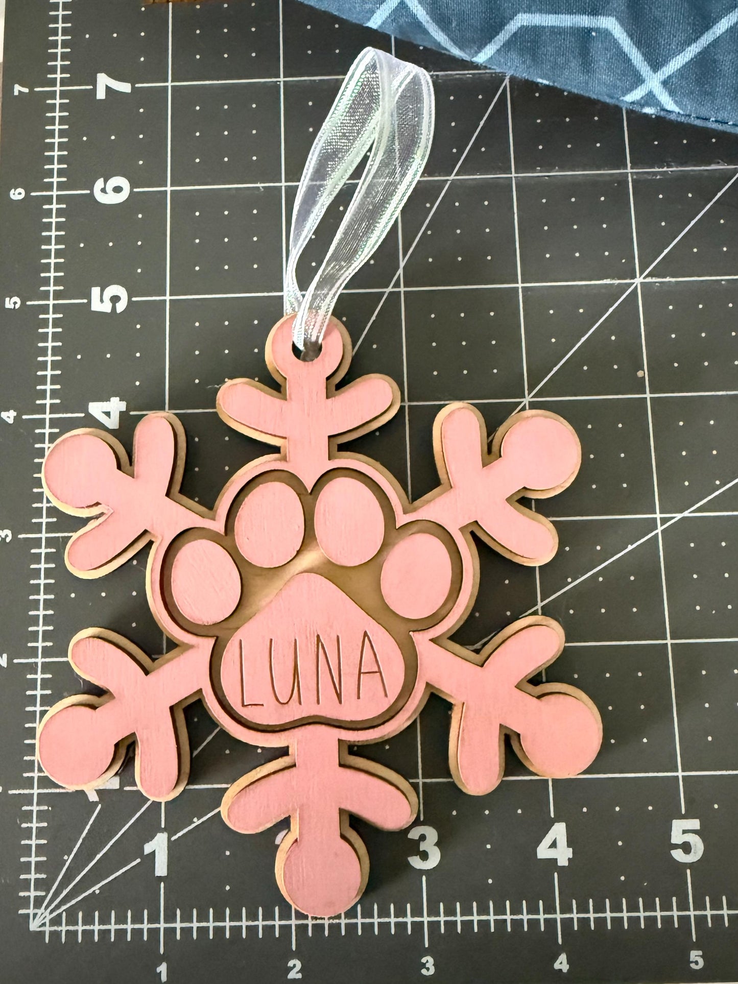 Personalized wooden dog paw snowflake ornament in pink with custom engraved pet name and white hanging ribbon, displayed as holiday décor