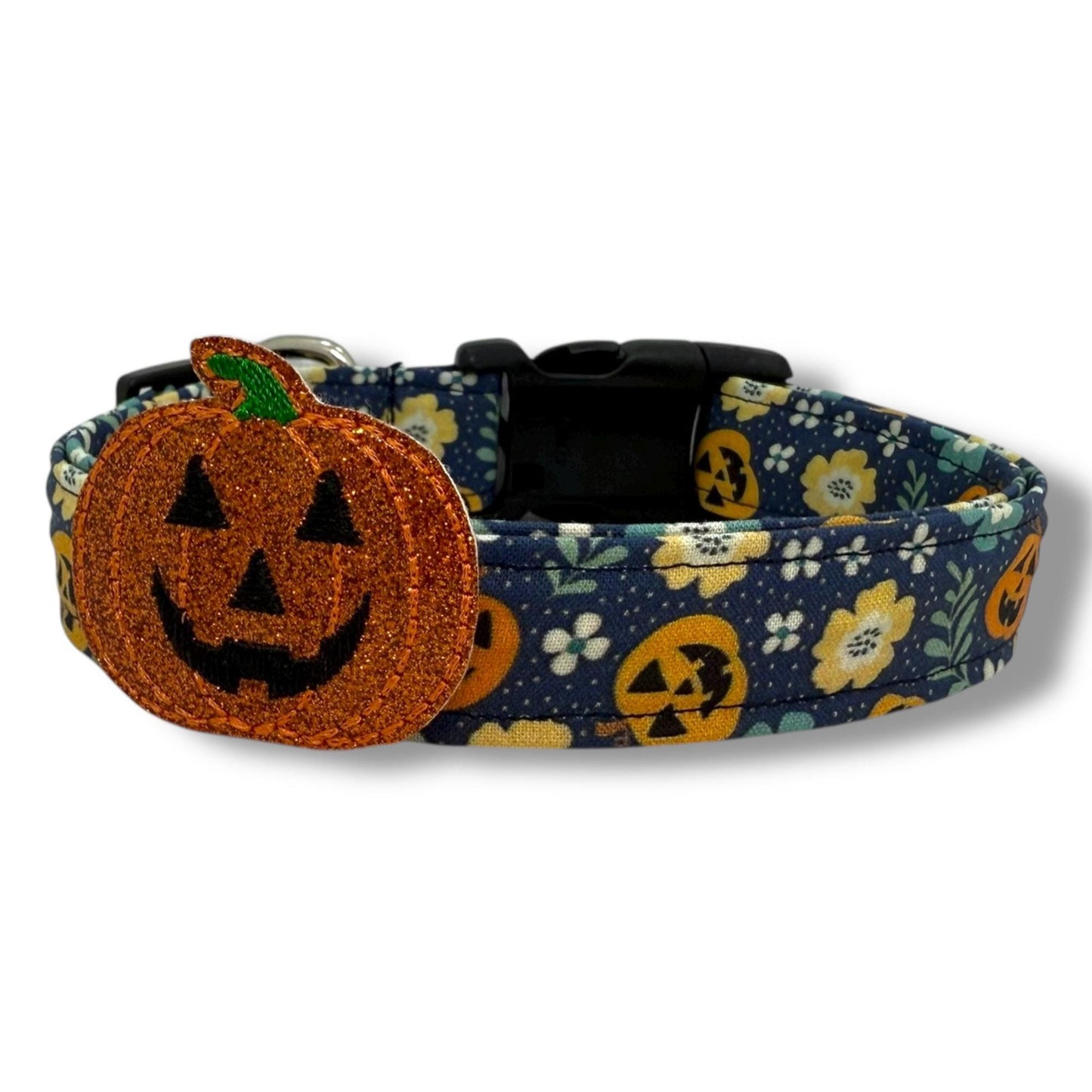 Halloween dog collar with jack-o’-lanterns, floral accents, and a removable shimmery pumpkin embellishment on a navy blue background.