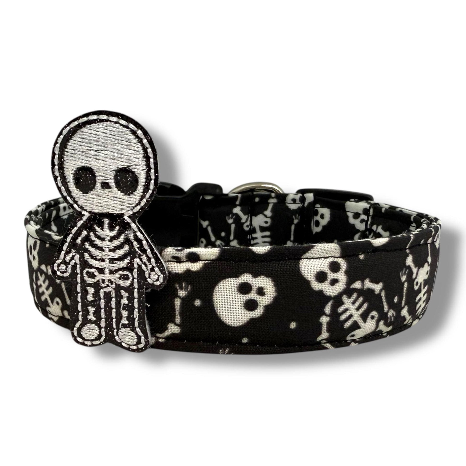 Halloween dog collar with skeletons and skulls on a black background, includes removable shimmery skeleton embellishment.