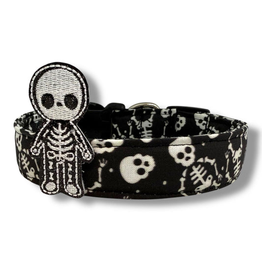 Halloween dog collar with skeletons and skulls on a black background, includes removable shimmery skeleton embellishment.
