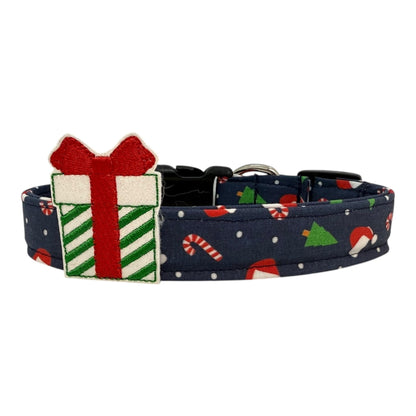 Navy cotton dog collar printed with small Christmas icons, featuring a Christmas gift embellishment, side-release buckle and metal D-ring, handmade and adjustable in multiple sizes.