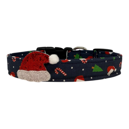 Navy cotton dog collar printed with small Christmas icons, with removable glitter Santa hat embellishment. The collar features a side-release buckle and metal D-ring, handmade and adjustable in multiple sizes.
