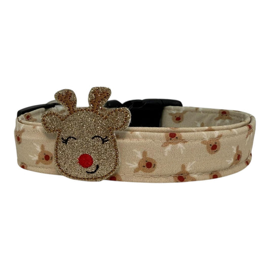 Beige dog collar with small red-nose reindeer faces and a removable shimmery reindeer embellishment, adjustable with black buckle and metal D-ring.